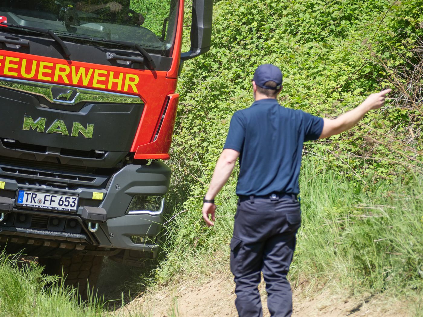 Ein Einweiser gibt dem Fahrer eines Feuerwehr-LKW Handzeichen an einem Hang