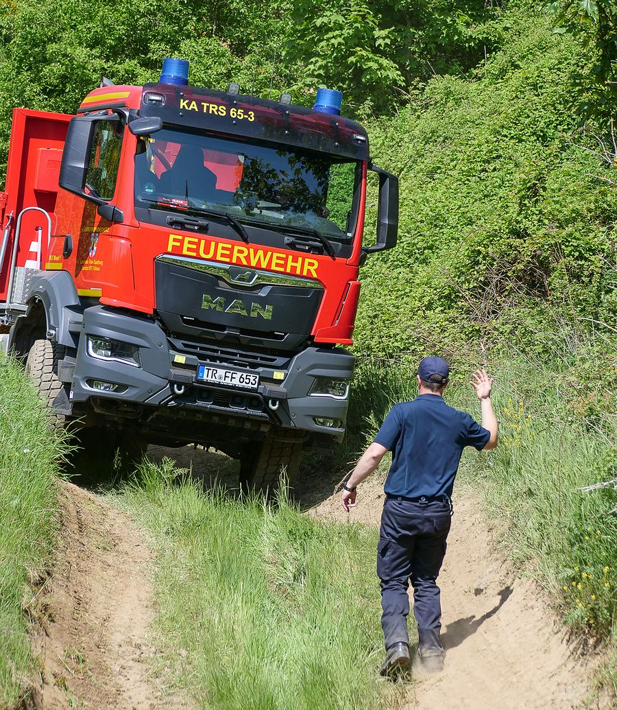 Einweiser geht vor einem Feuerwehr-LKW her und gibt Handzeichen bei der Abfahrt im Gelände